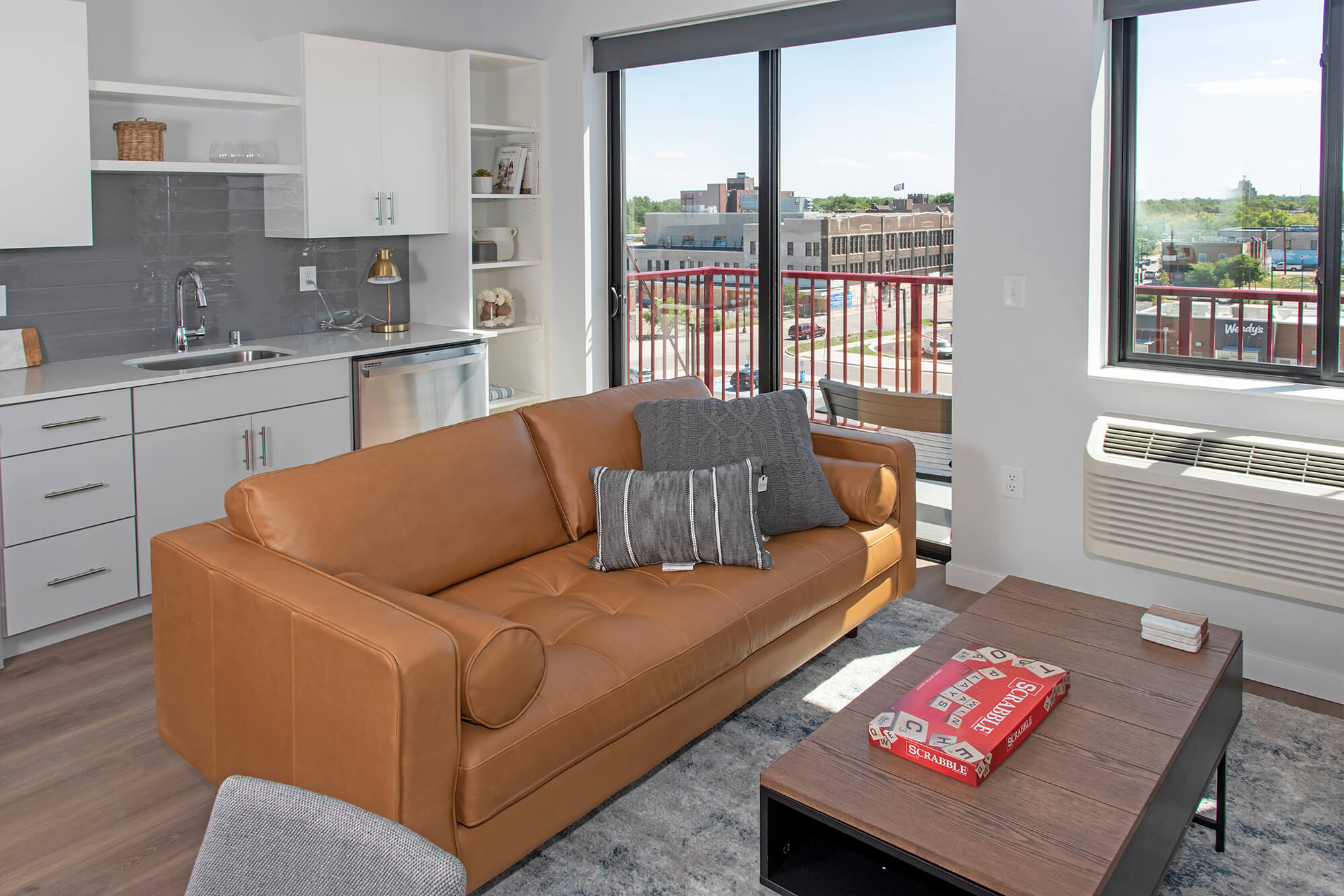 Open-concept apartment living area with leather sofa, kitchen, and balcony views.