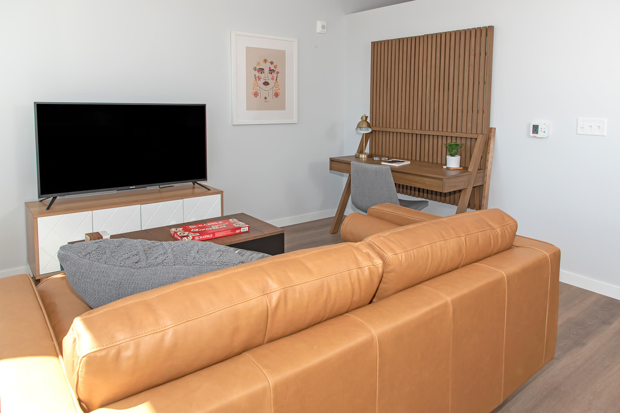 Apartment living room with leather sofa, TV console, and compact desk area.