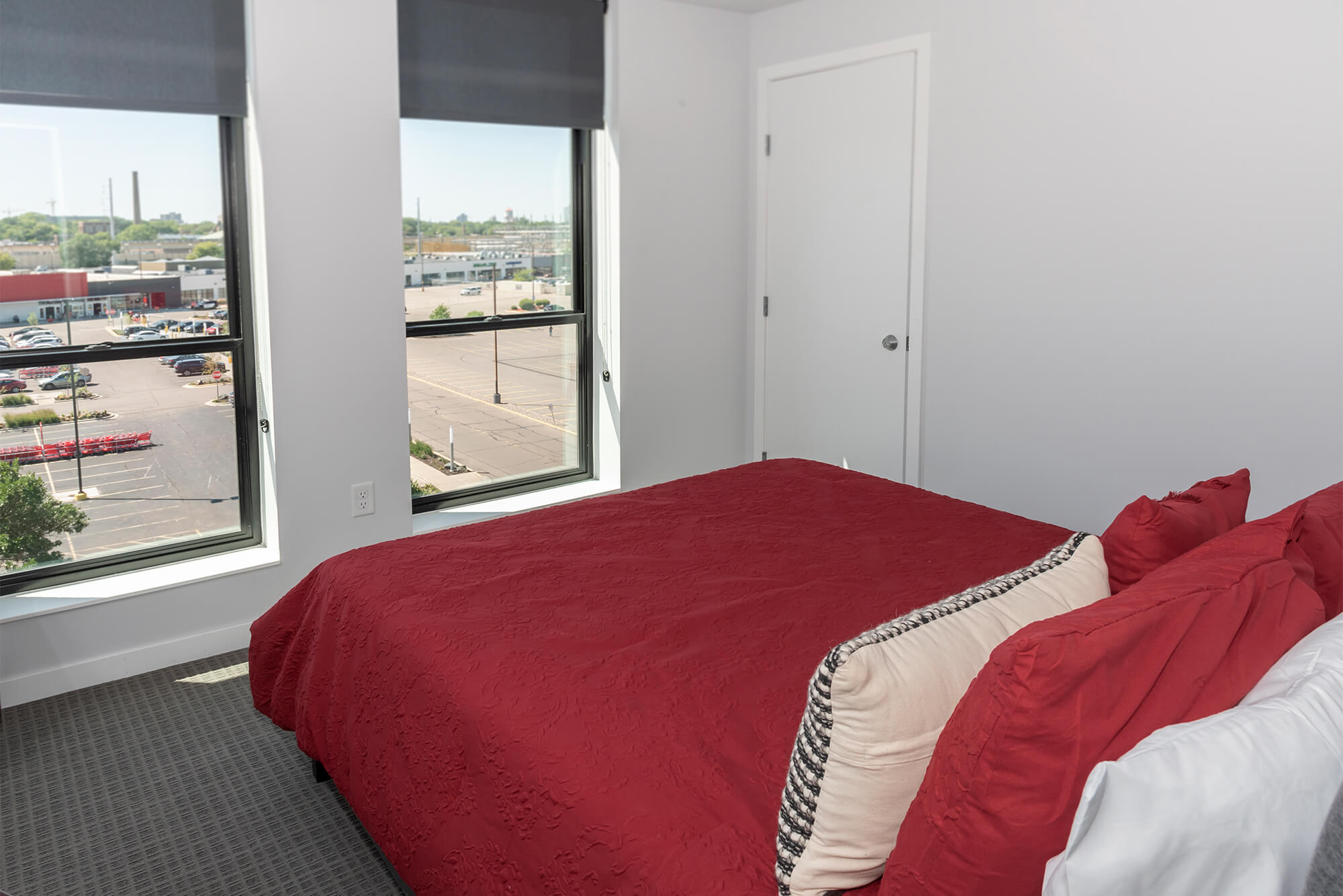 Bedroom with red bedding, large windows, and neighborhood views.
