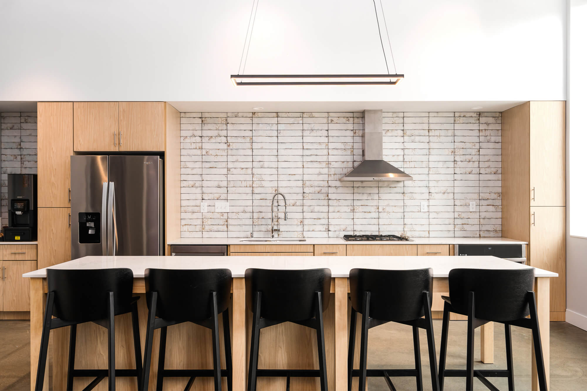 Shared community kitchen with large island seating, stainless steel appliances, and wood cabinetry.