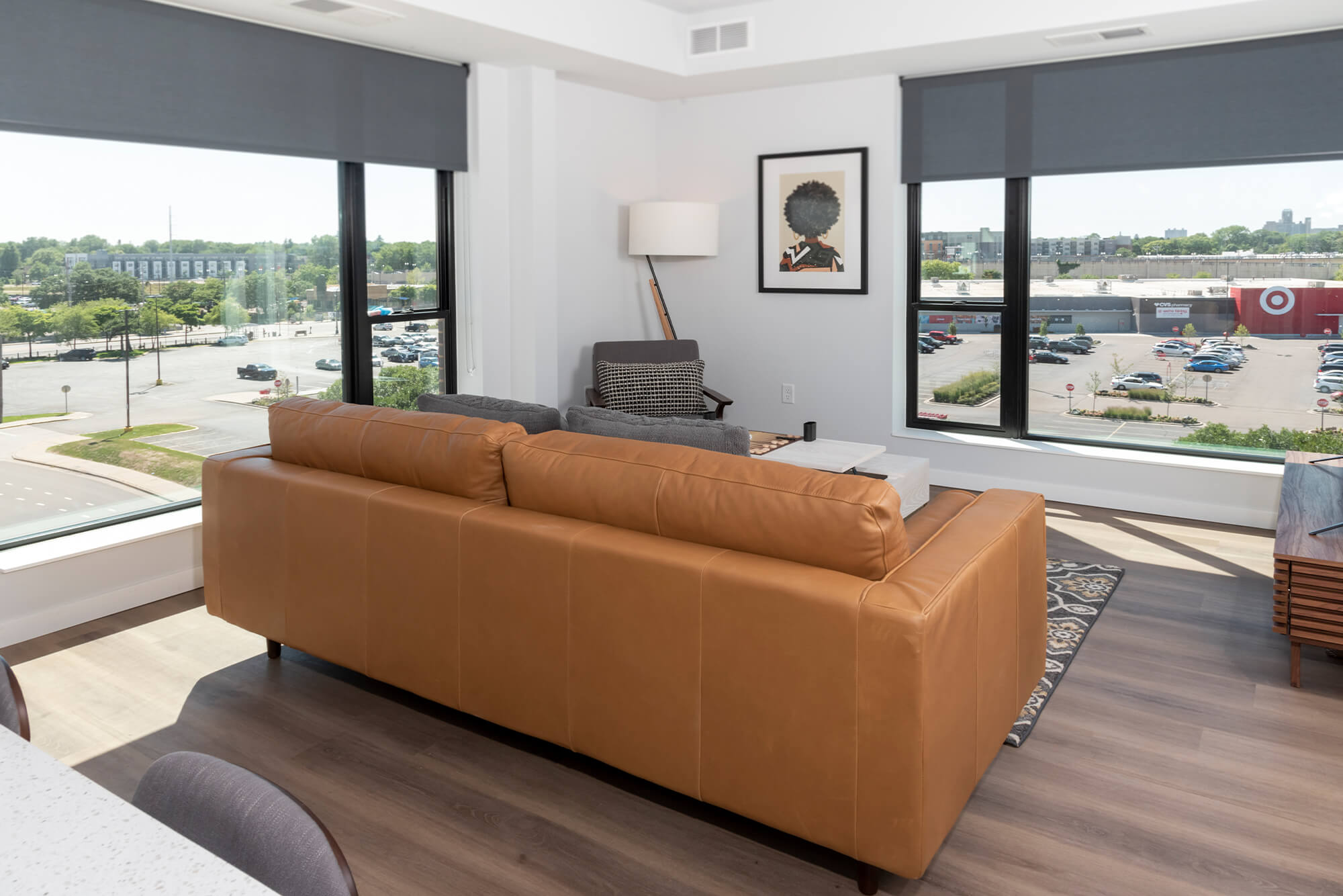 Bright living room with a leather sofa, accent chair, coffee table, and large corner windows.