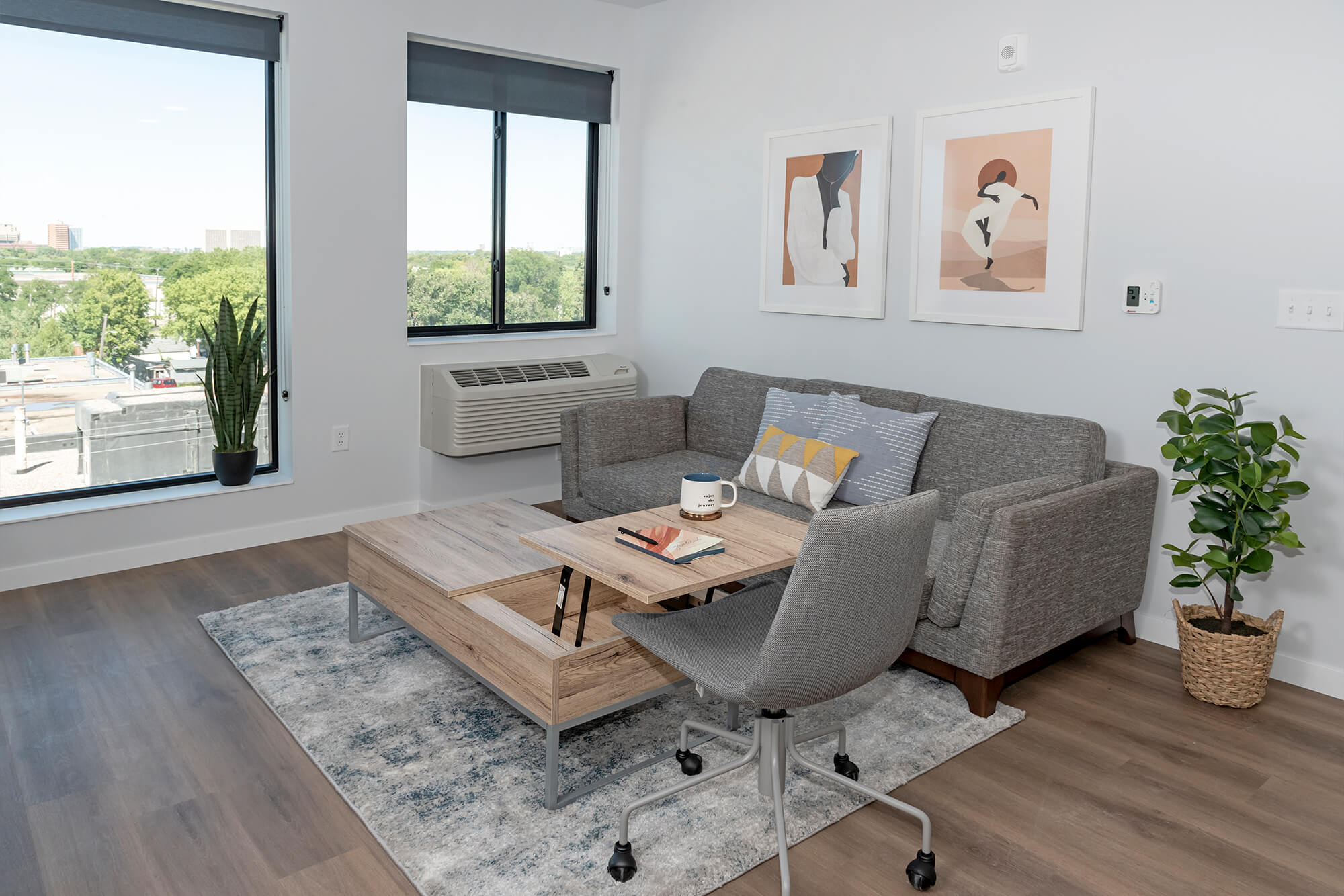 Bright living room with a gray sofa, coffee table, desk chair, and large windows.