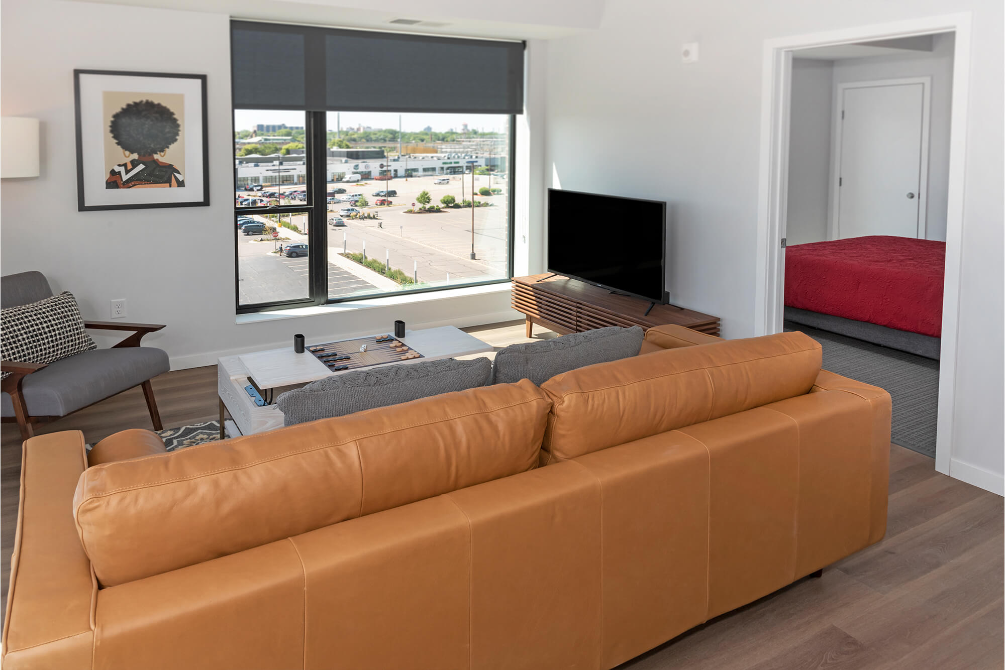 Living room with leather sofa, TV console, accent chair, and bedroom visible through the doorway.