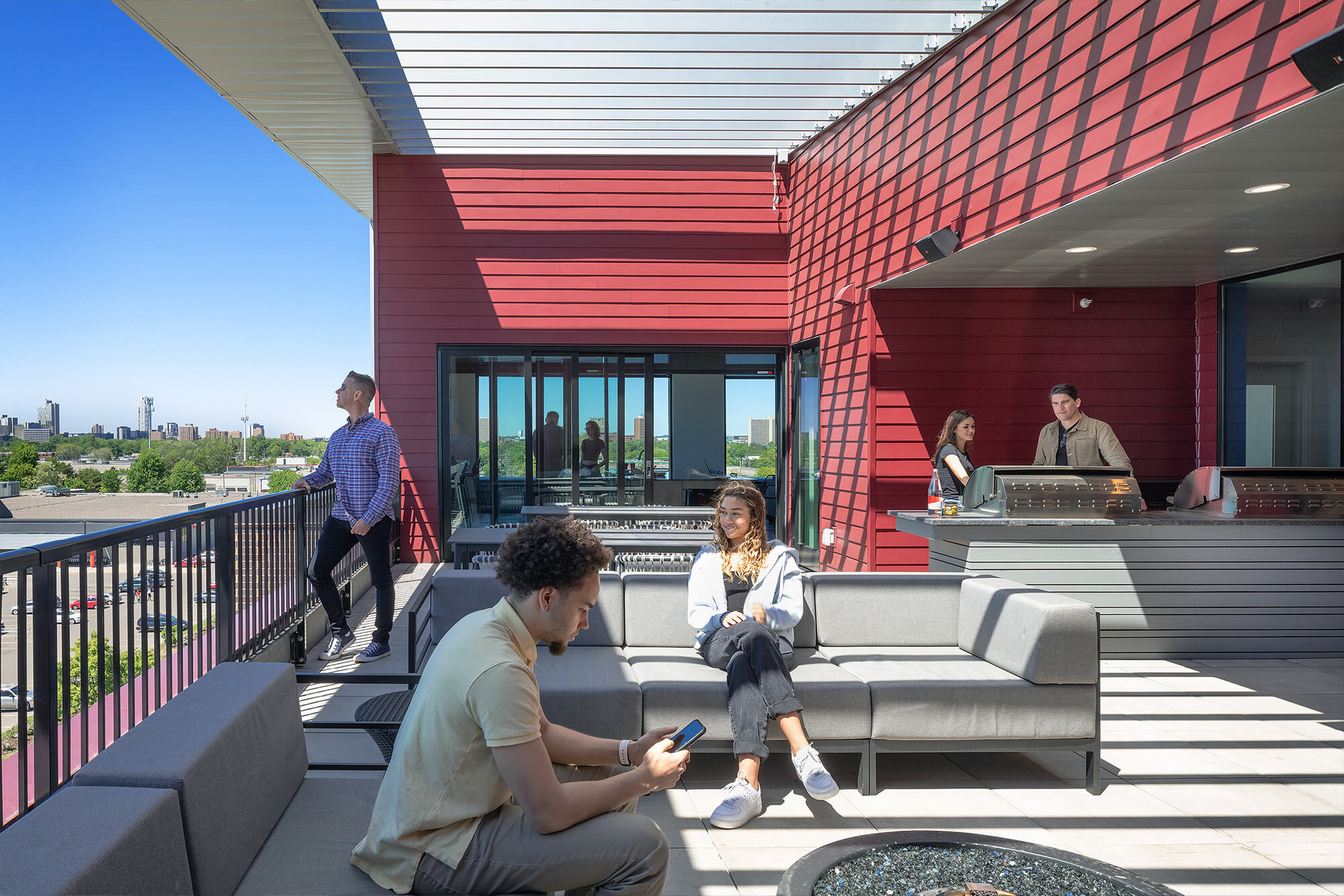 Residents relaxing on the rooftop terrace with lounge seating, grilling stations, and Minneapolis skyline views.