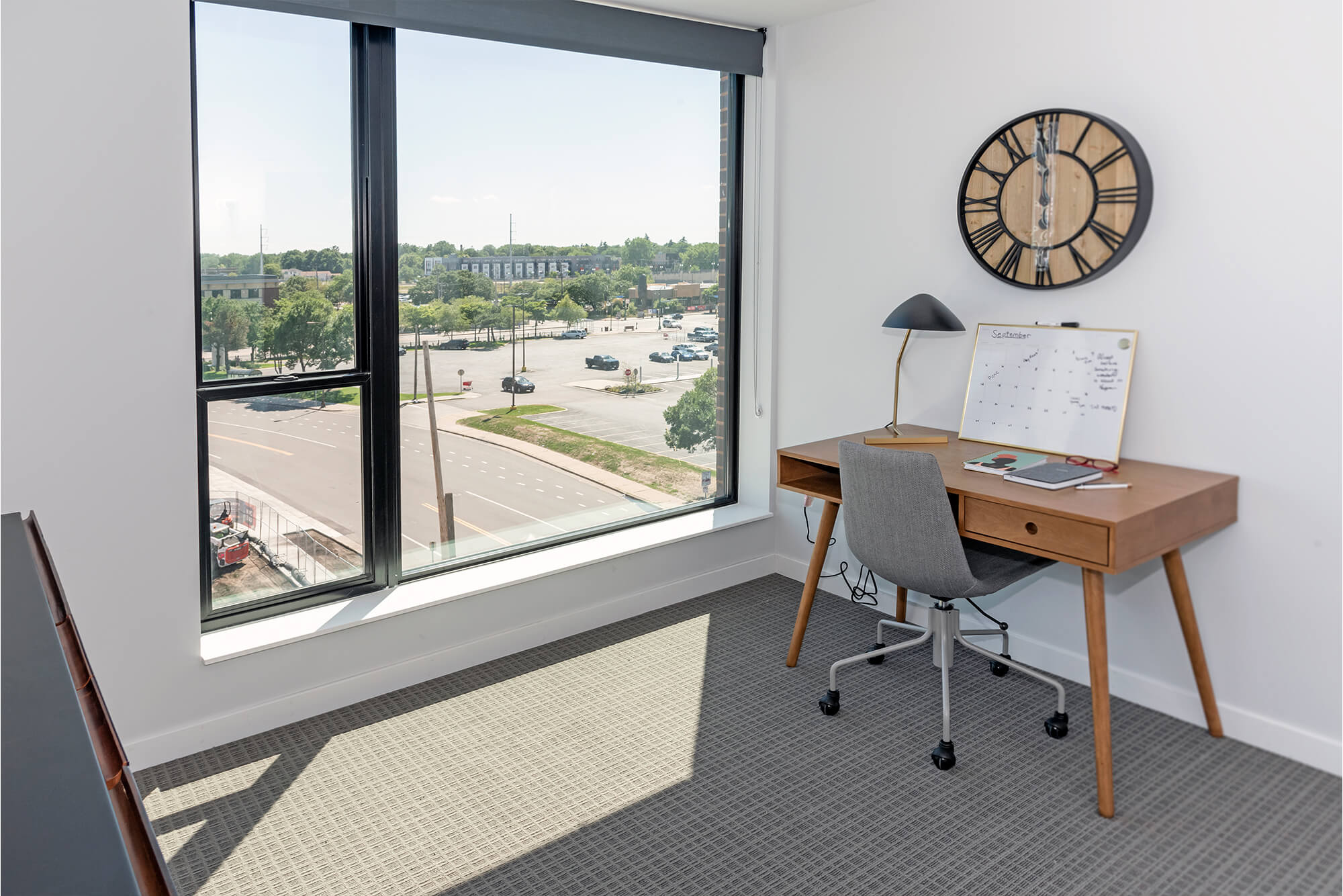 Home office area with desk, chair, wall clock, and large window with neighborhood views.