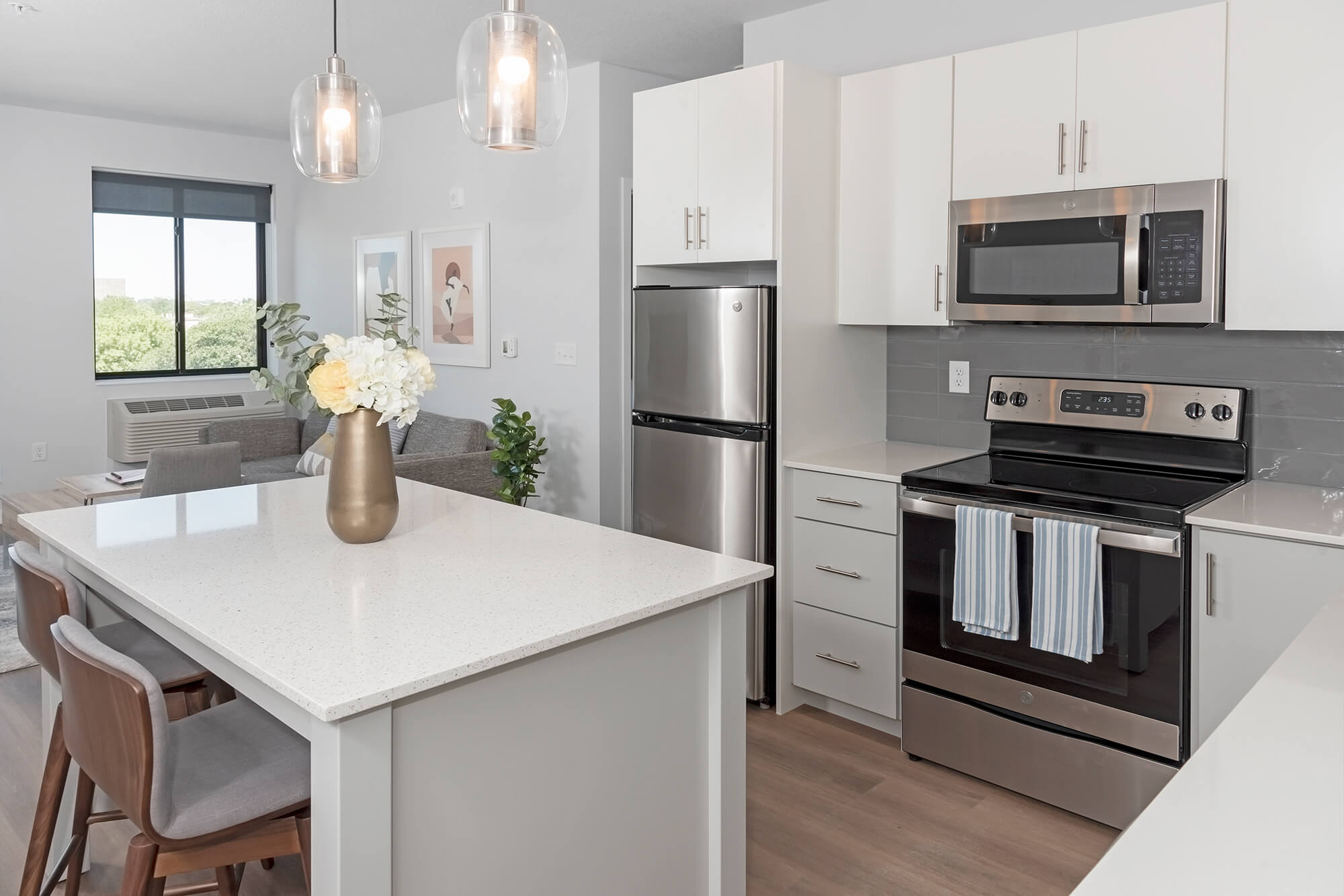 Modern apartment kitchen with white cabinets, stainless steel appliances, and island seating.